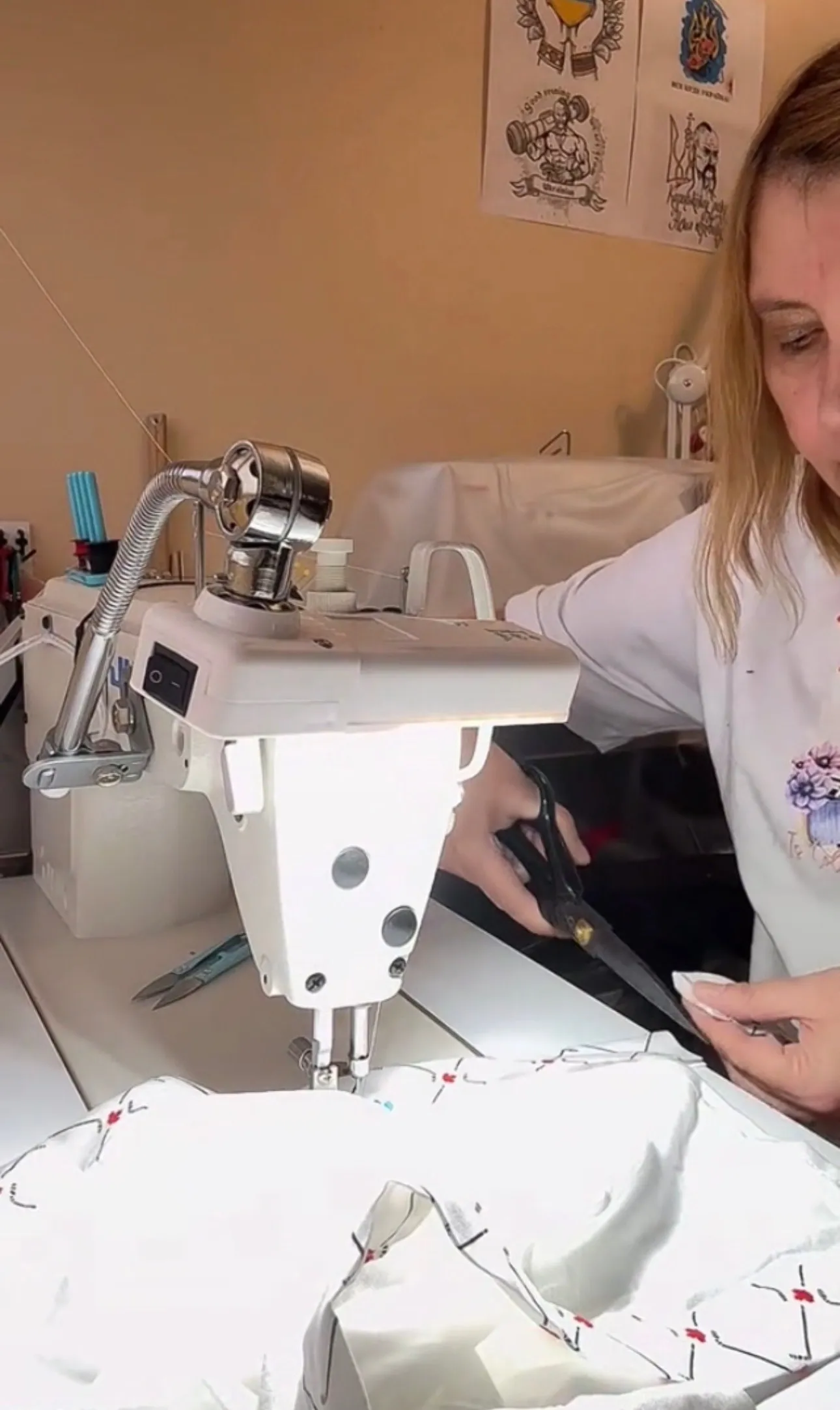 Alla trimming thread at the industrial machine, white fabric pinned in front of her.